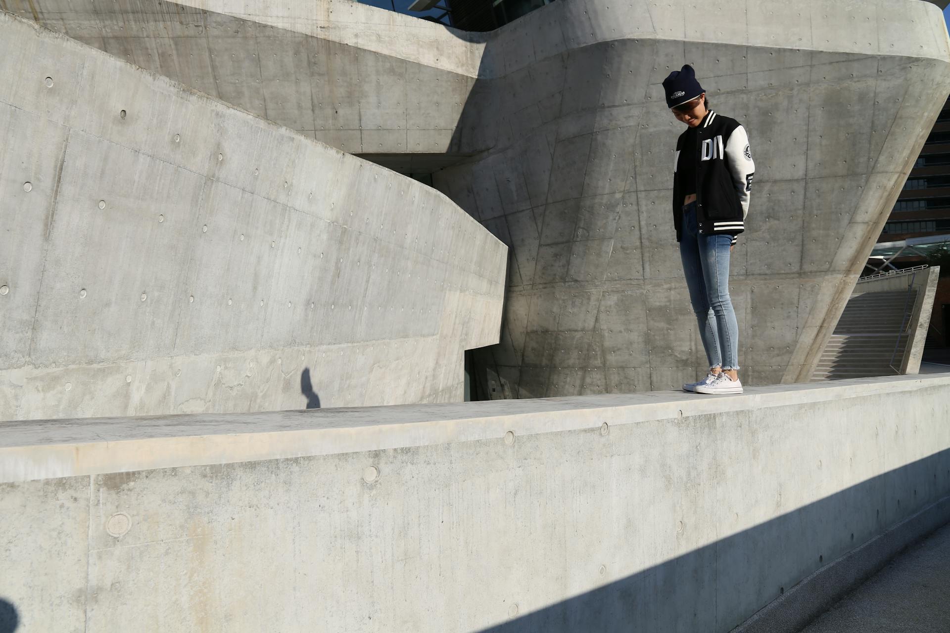 Woman in casual wear stands outdoors on modern concrete structure, creating urban vibe.