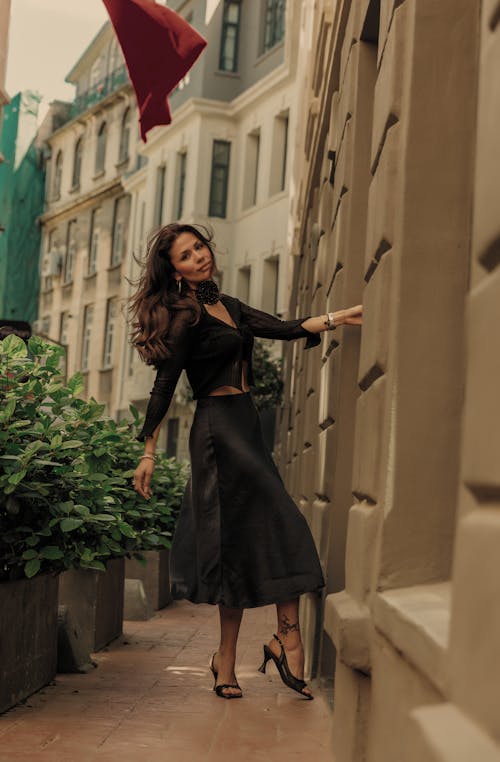 A woman in a black skirt and top is leaning against a wall