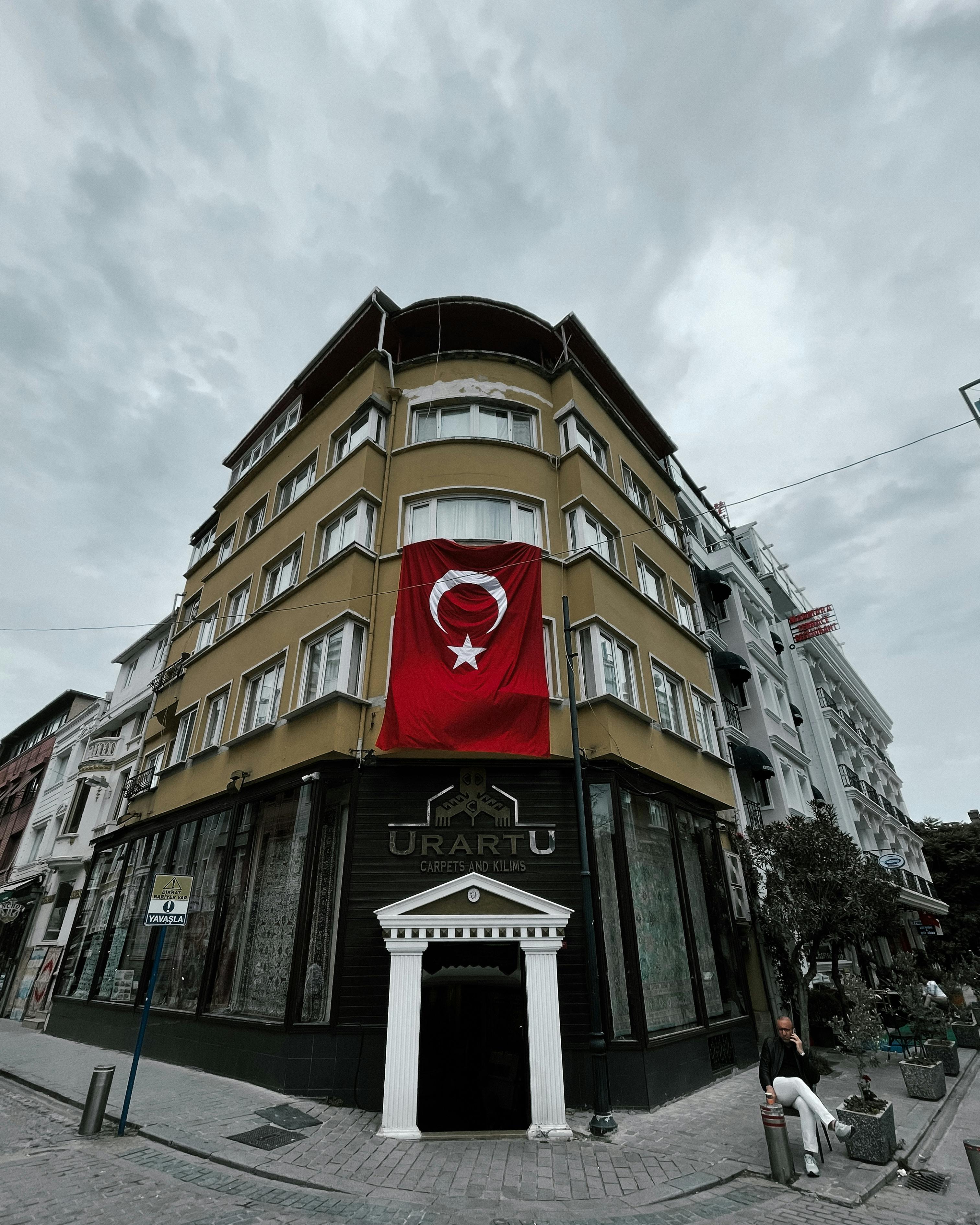 Free A building corner featuring a large Turkish flag over a shop entrance in a cityscape. Stock Photo