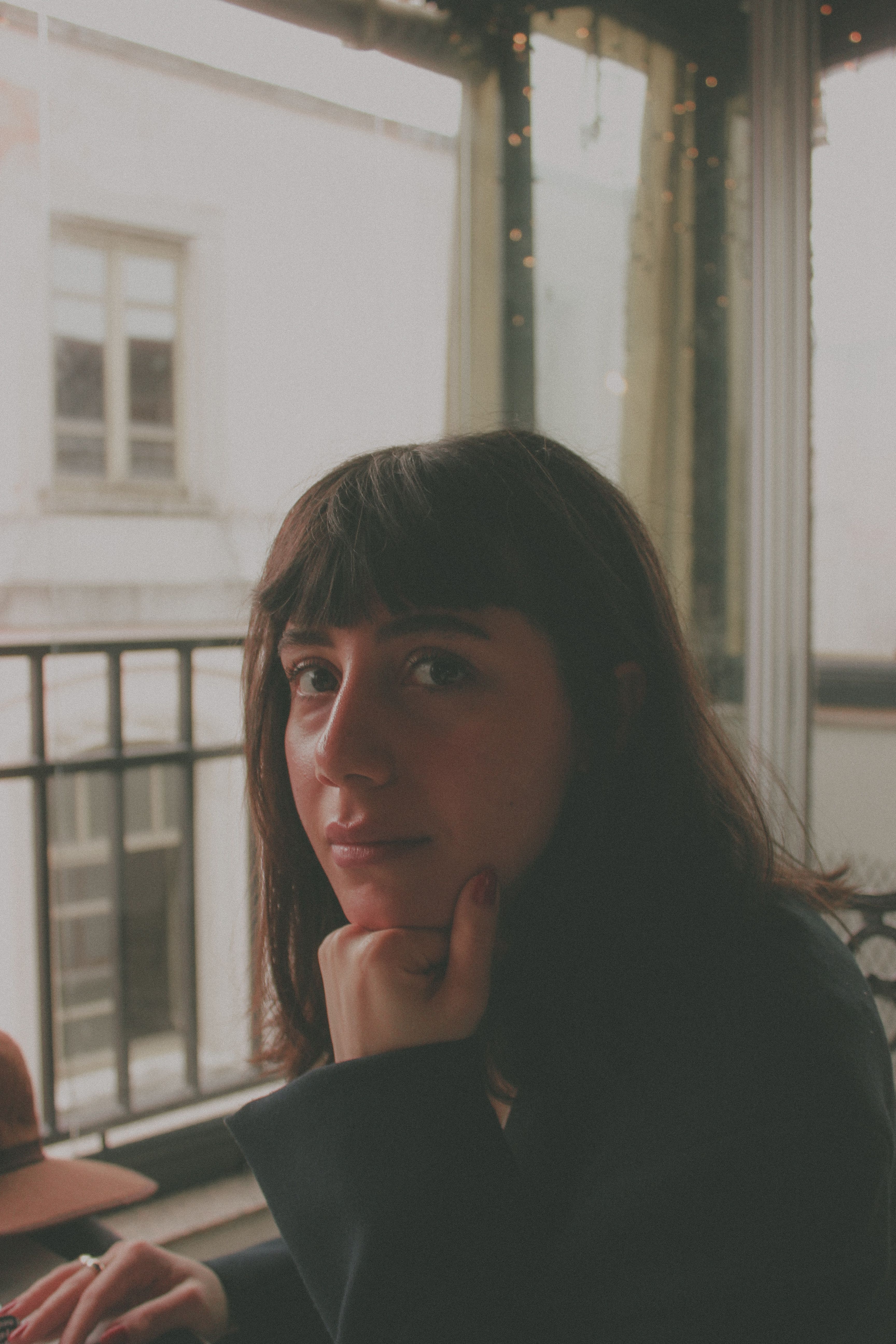 Warm indoor portrait of a woman sitting by a window with city view.