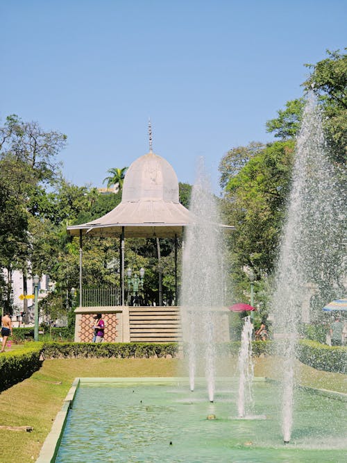 A fountain in a park with a gazebo in the background