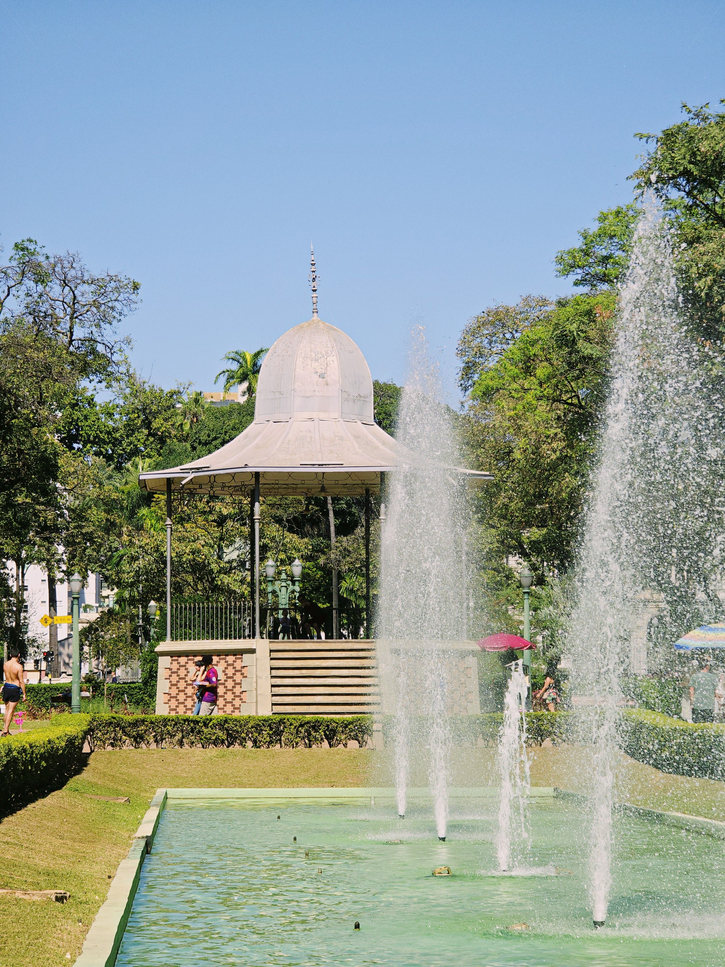 A fountain in a park with a gazebo in the background · Free Stock Photo