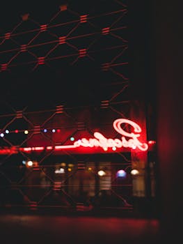 A moody capture of a neon sign glowing through a grid in an urban setting at night.
