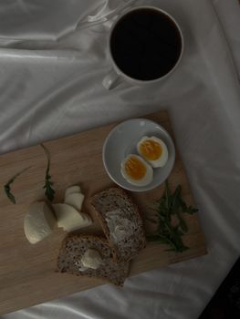 Top view of bread, cheese, and eggs on a wooden tray with tea.
