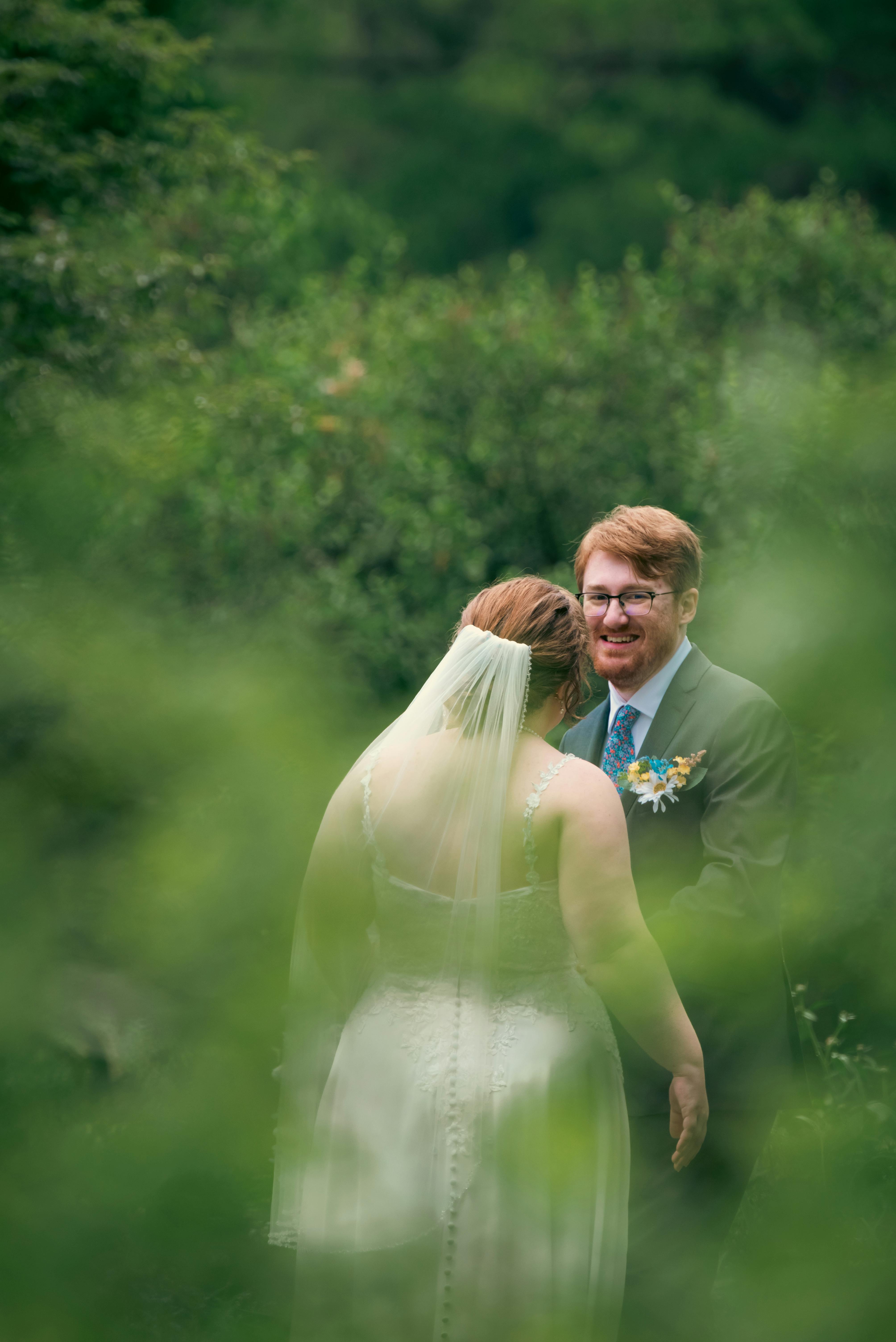 Bride and groom share a tender moment surrounded by lush greenery.