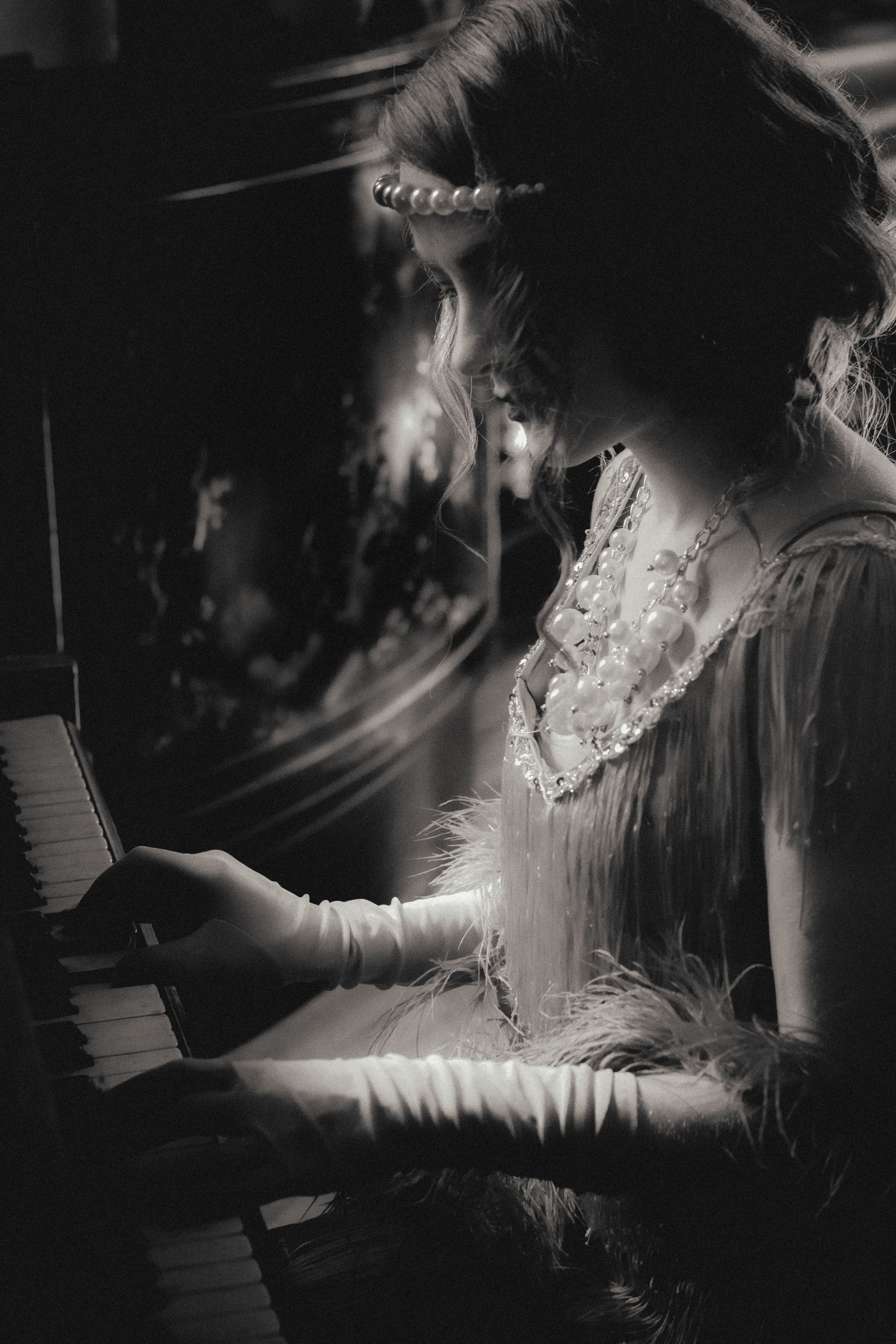 Black and white photo of a woman in a flapper dress playing piano, exuding vintage elegance.