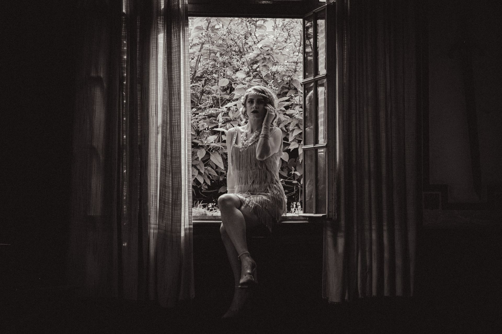Elegant black and white portrait of a woman in a flapper dress, sitting in a window sill.