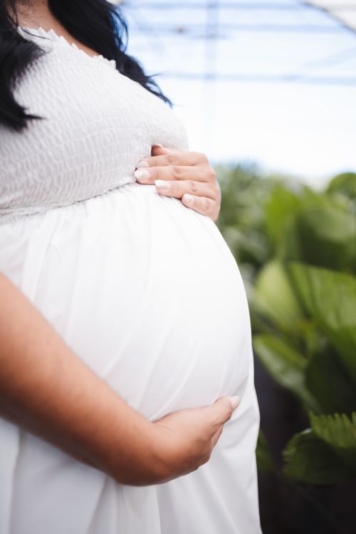 Free Pregnant woman in white dress holding belly in an outdoor setting, capturing the essence of motherhood. Stock Photo