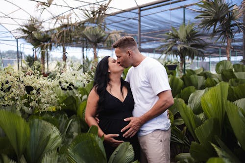 A pregnant woman and her husband are standing in a greenhouse