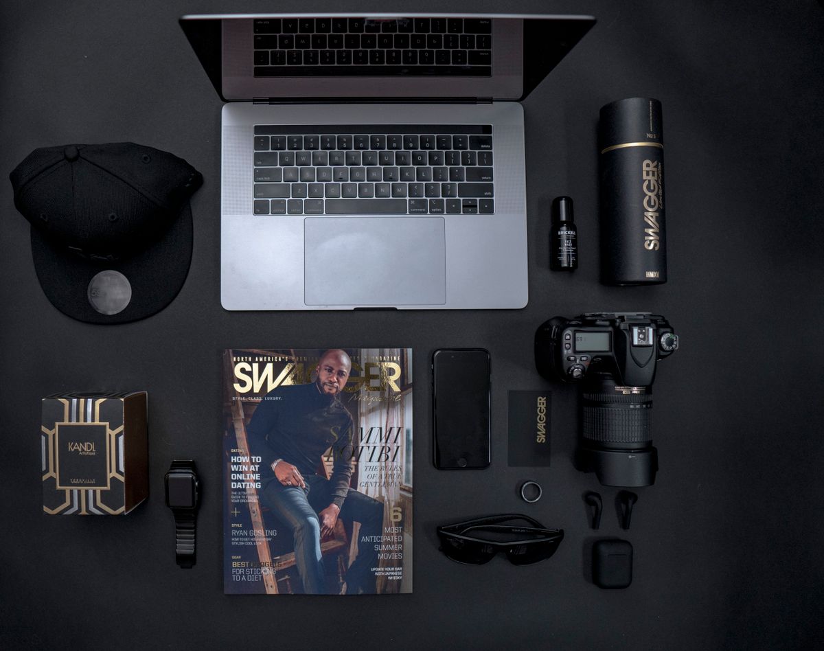 A laptop, camera and magazine laid out on a dark desk