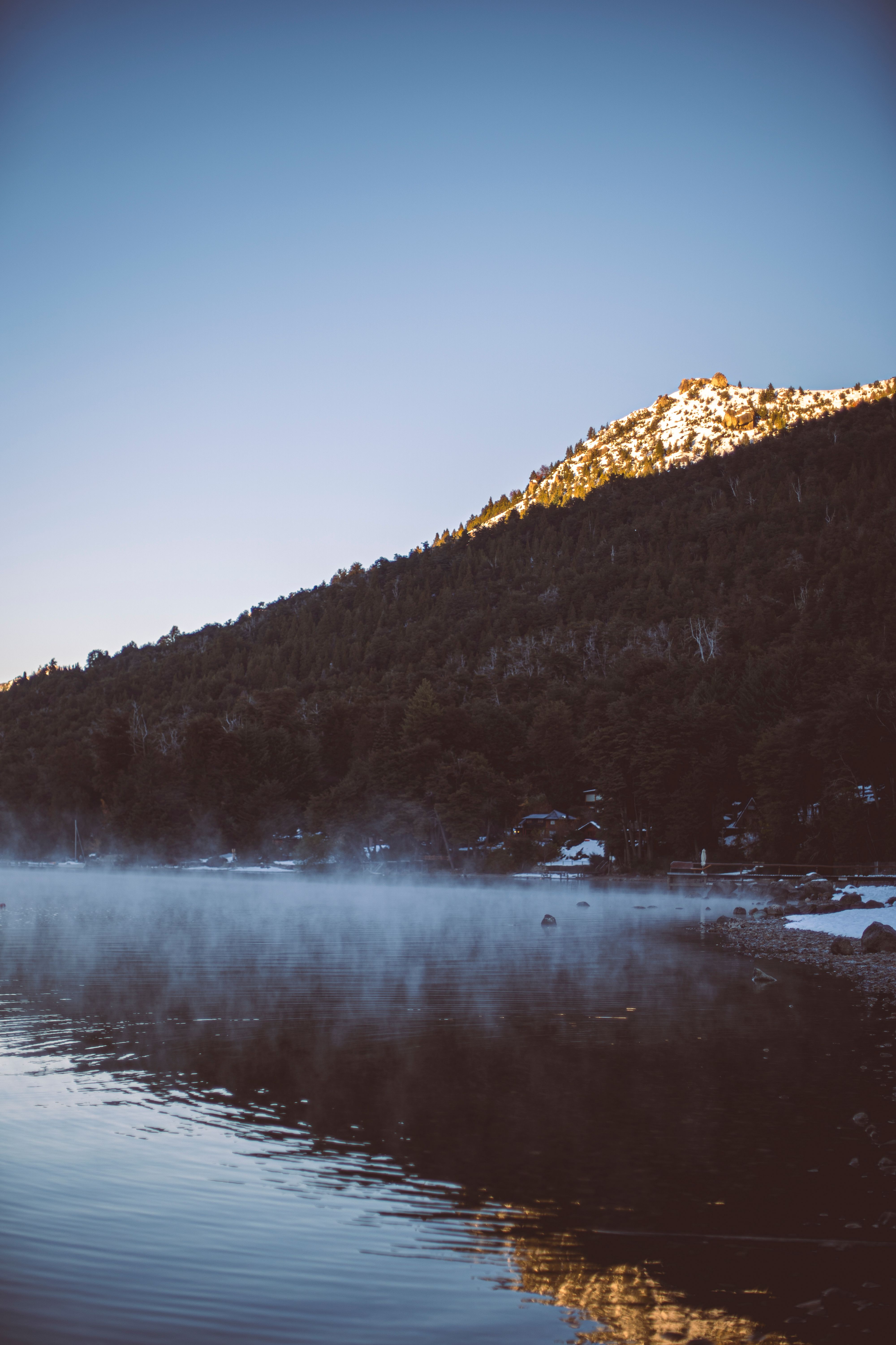Mist rises over a tranquil lake with mountain backdrop in Bariloche, Argentina.