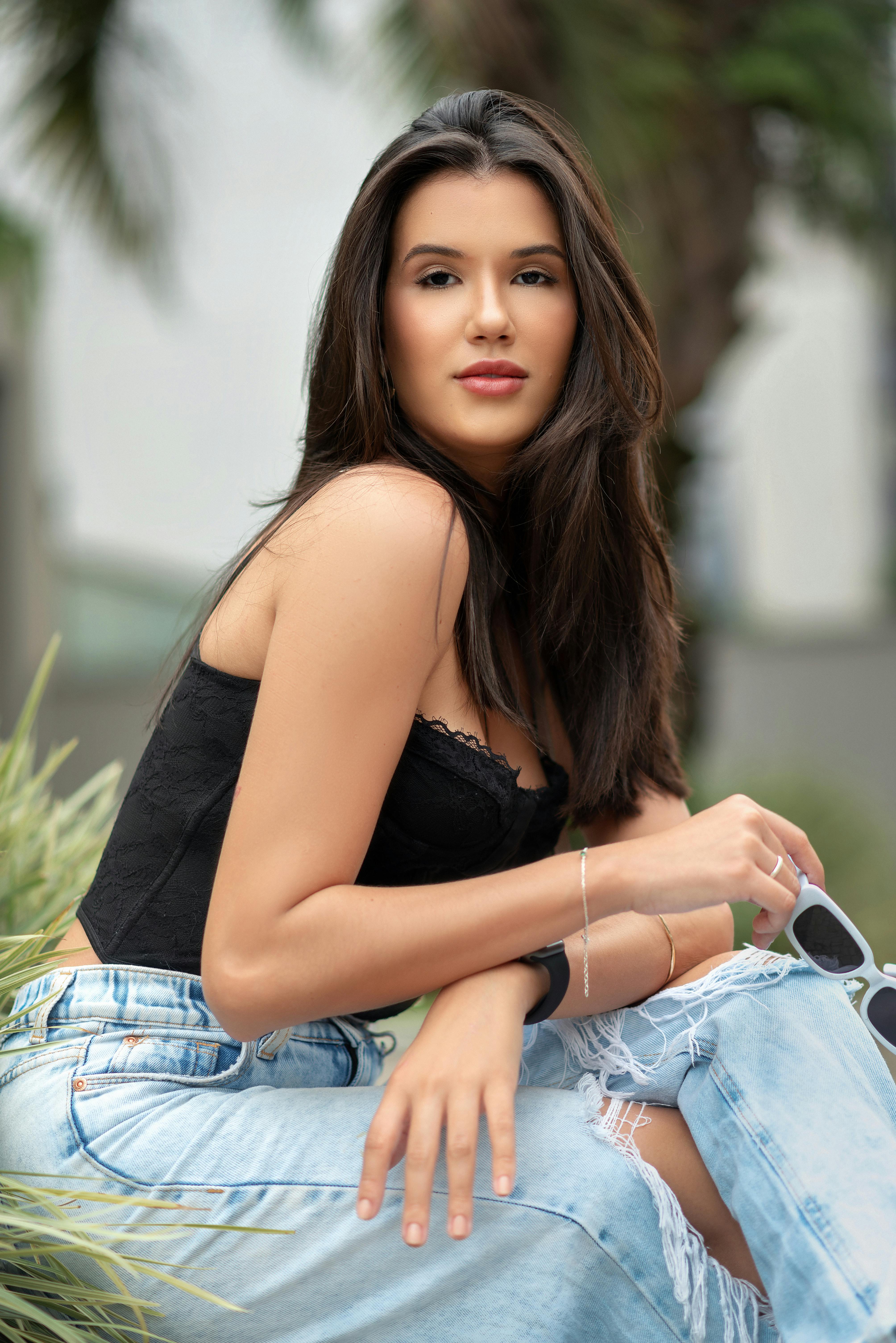 Fashionable young woman posing outdoors in Nova Lima, wearing a black top and ripped jeans.