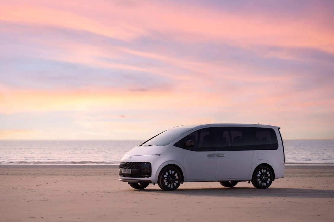 Free The sea under a pink sunset and the left front side view of the Hyundai Staria Hybrid. Stock Photo