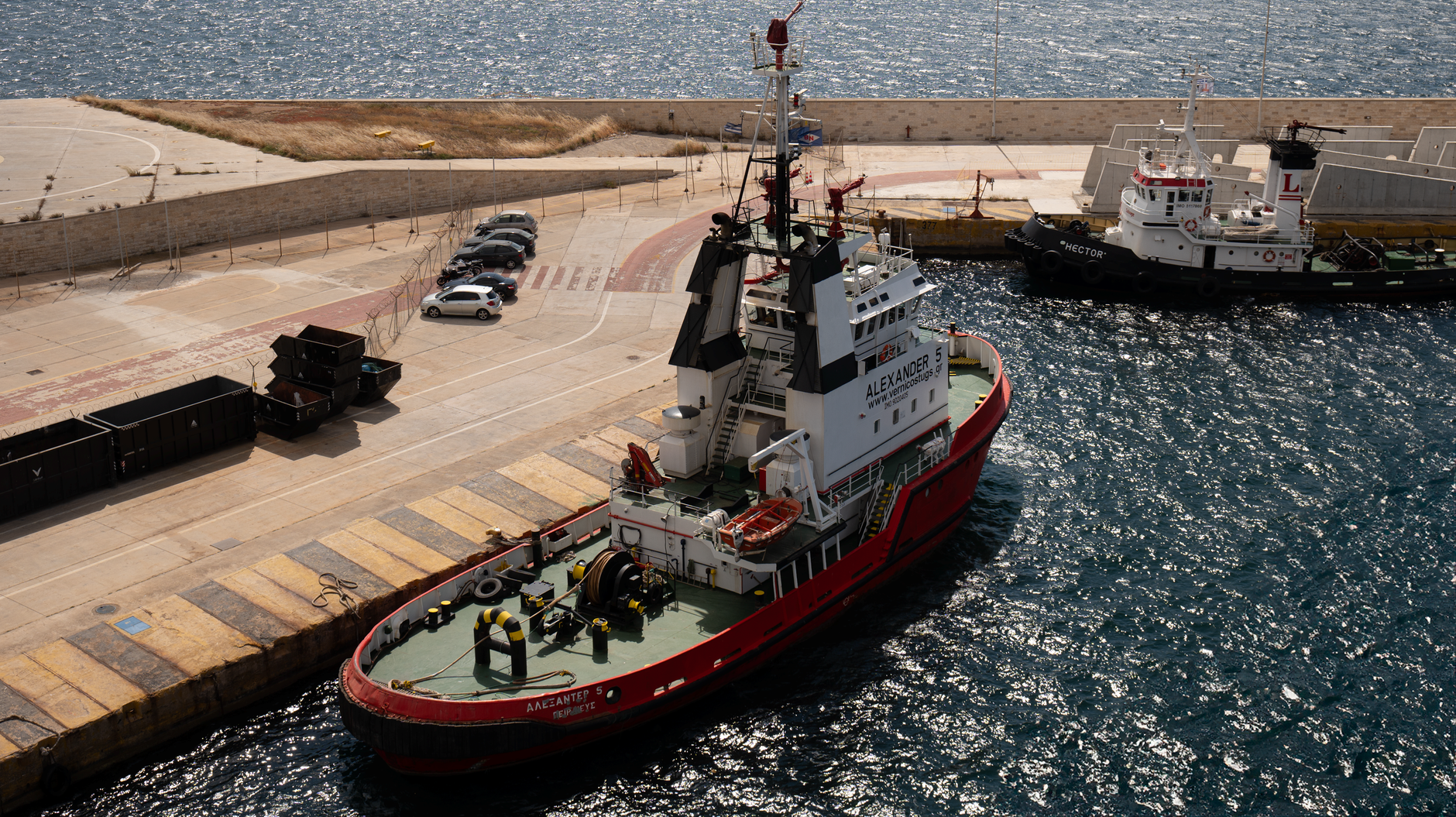 Aerial view of a harbor featuring tugboats and docks under a sunny sky.