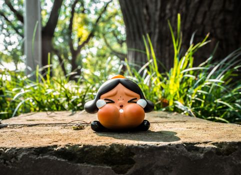 Adorable cartoon figurine on a stone surrounded by lush green grass in sunlight.