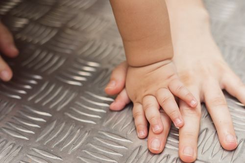 Free A tender close-up capturing a baby's hand gently touching an adult's hand on a metallic background. Stock Photo