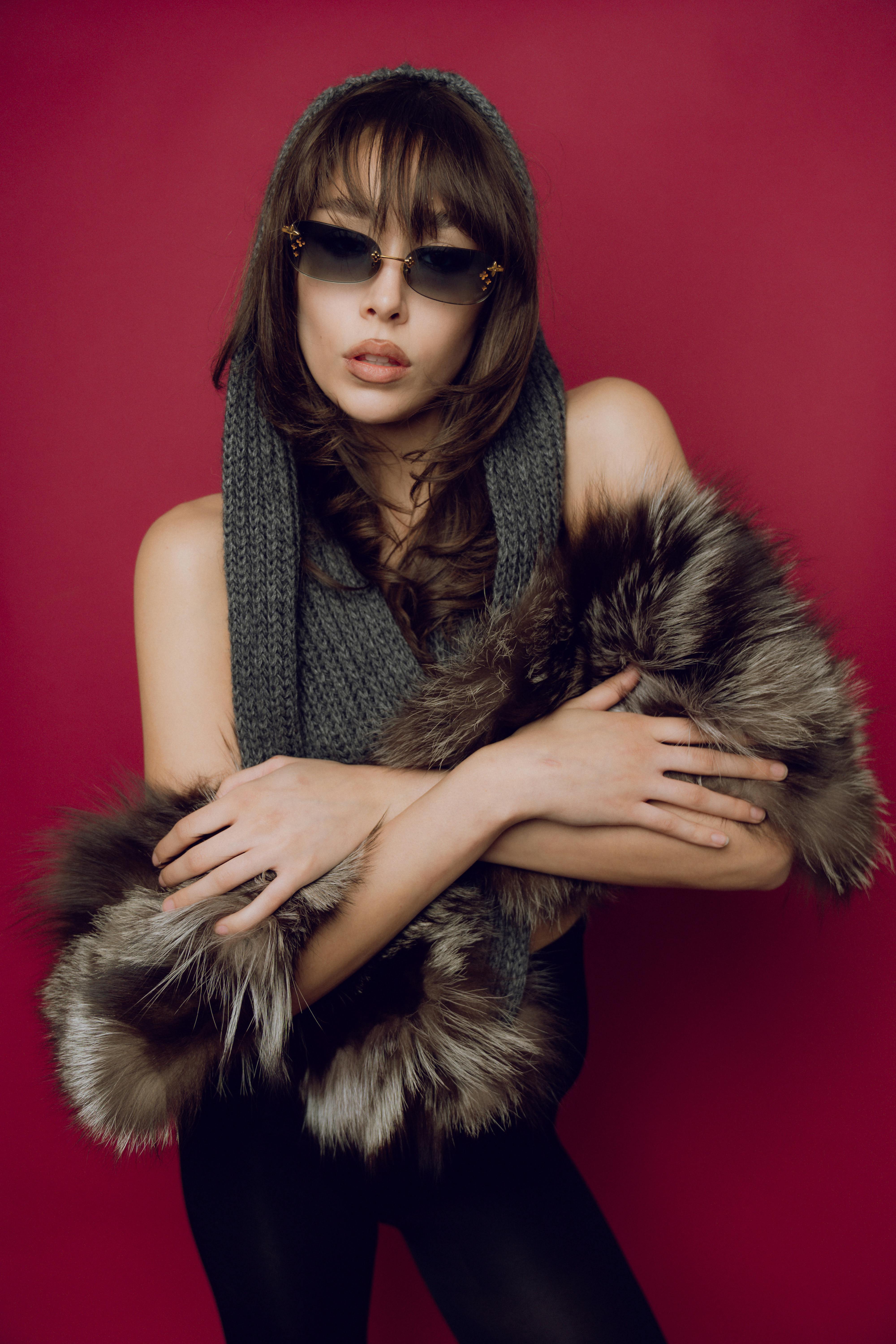 a woman in glasses and fur coat posing for a photo