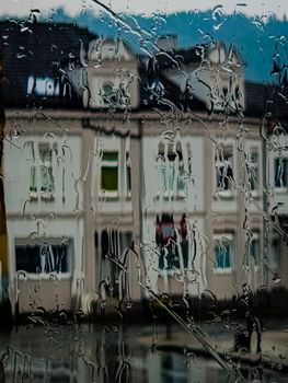 Raindrops on a window create a blurred view of townhouses in Velbert, Germany, capturing the urban rainy atmosphere.