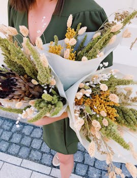 光天化日之下，一名身穿绿色连衣裙的女子拿着两束精致的花束走在石路上