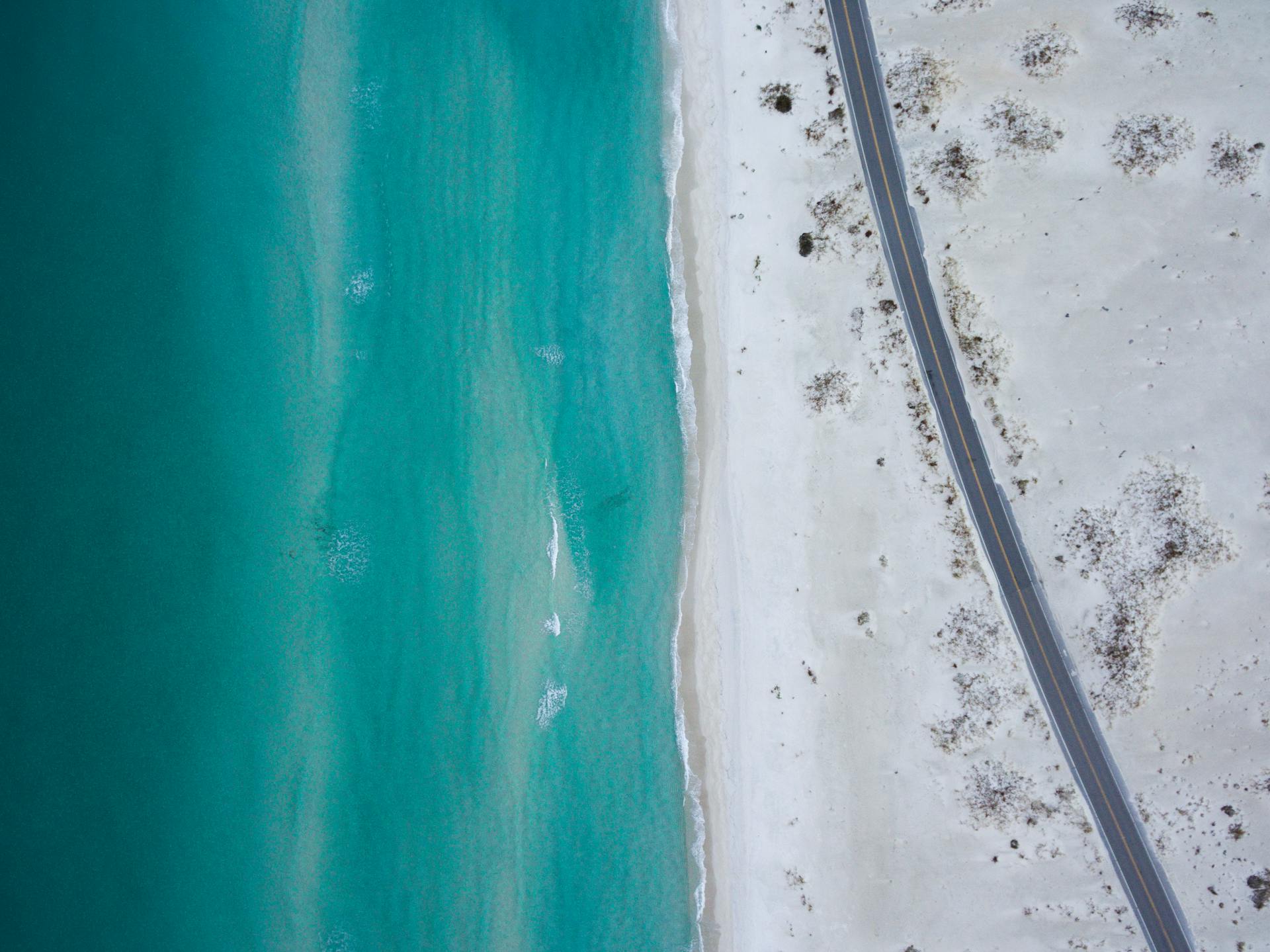 A stunning aerial shot capturing a deserted coastline with azure waters and an empty road parallel to the sand.