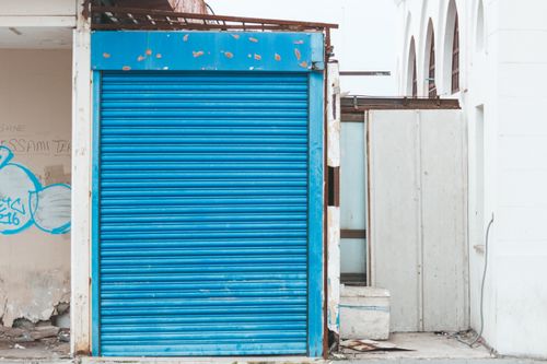 Free A blue roller shutter on a decayed building facade, featuring graffiti and signs of decay. Stock Photo