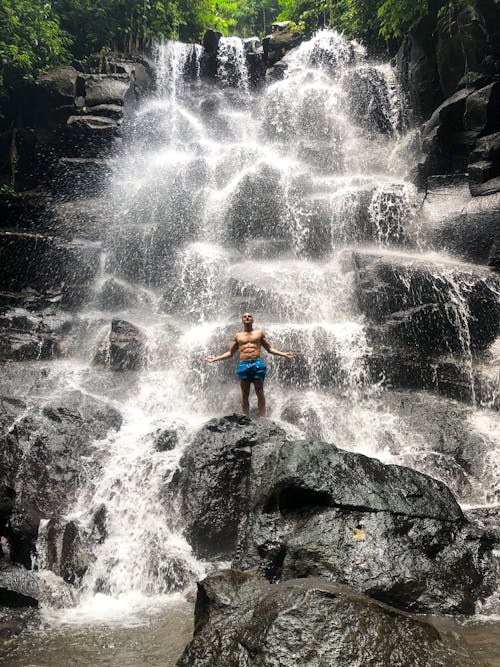 Hombre En Topless De Pie Sobre Una Roca En El Centro De Una Cascada