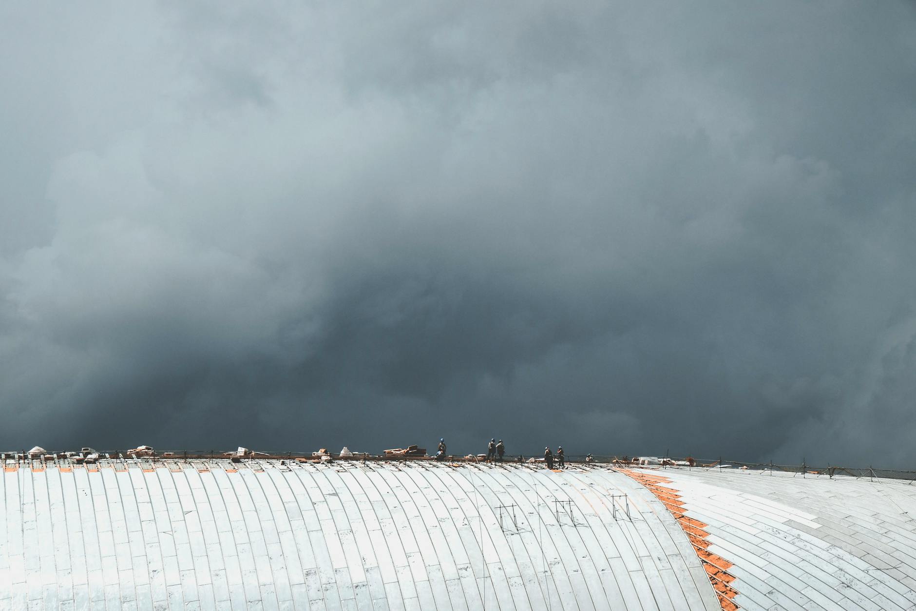 Workers on a rooftop performing maintenance under dark stormy skies, highlighting industrial resilience.