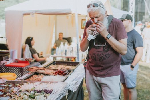 Senior man with a beard enjoying street food at an outdoor market festival.