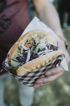 A delicious doner kebab wrap filled with fresh vegetables, held outdoors under sunlight.