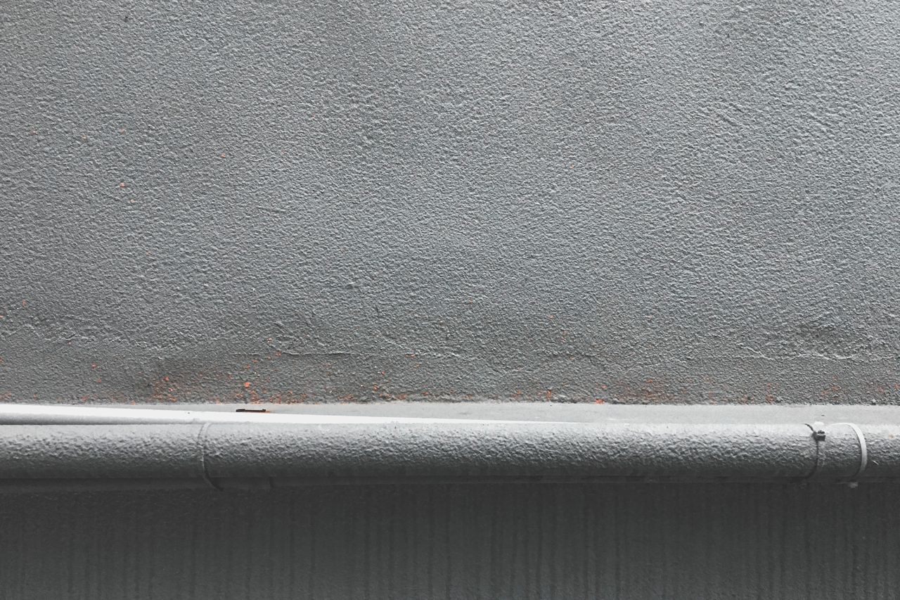 close up of a textured grey concrete wall with a metal pipeline along