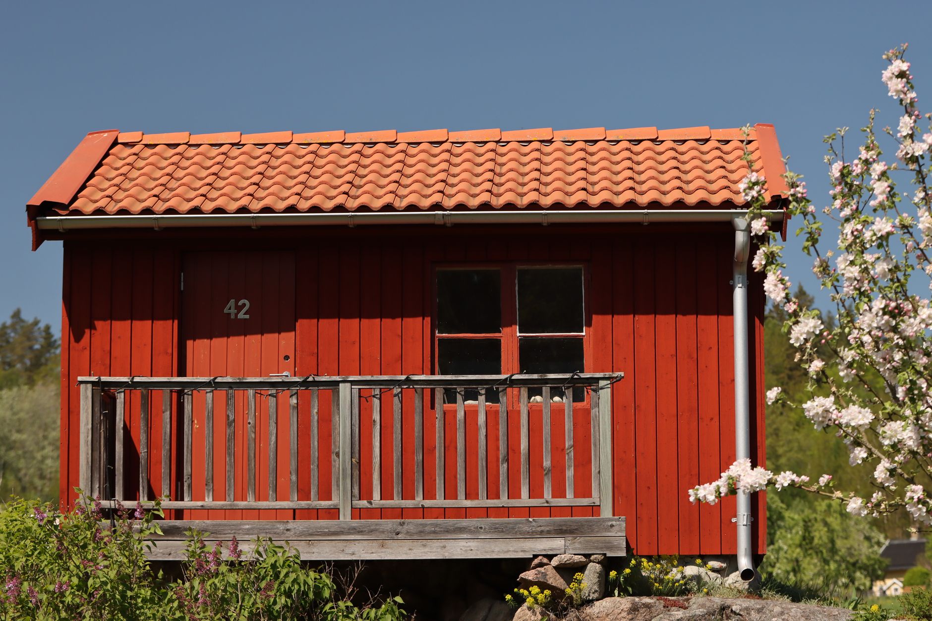 Rött trähus i trädgård – exempel på komplementbyggnad i svensk villabebyggelse