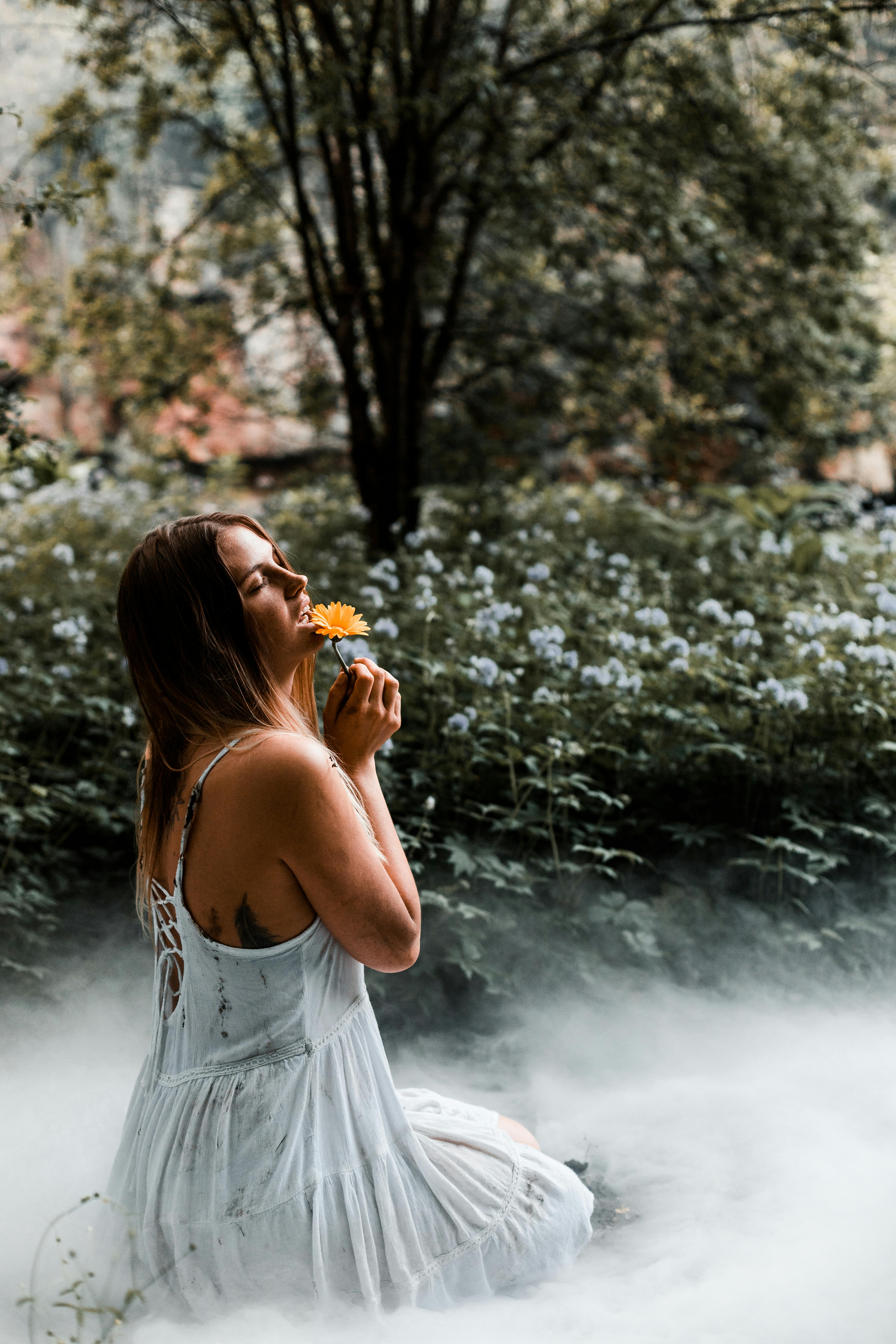 一名女子身穿白色连衣裙，在梦幻般的雾气森林中捧着鲜花