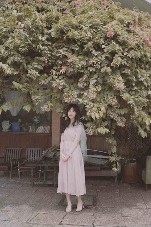 A woman in a pink dress stands under a tree