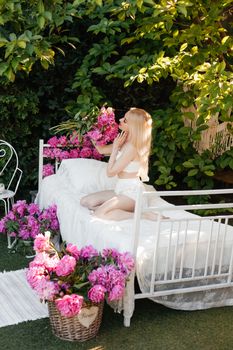 Blonde woman in a bed surrounded by pink flowers, enjoying a sunny garden scene.
