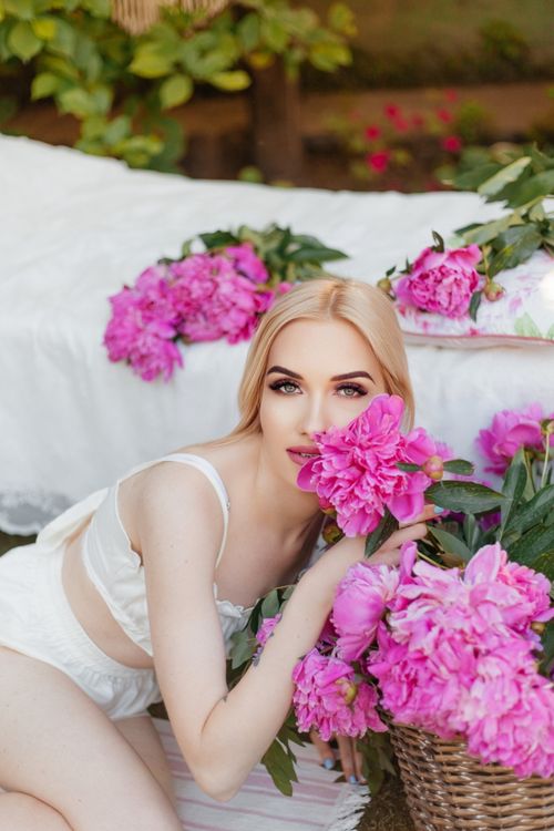 Free A serene portrait of a woman surrounded by vibrant pink peonies, exuding summer elegance and natural beauty. Stock Photo