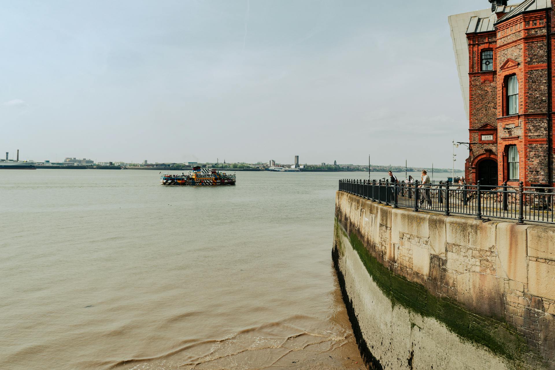 View of Liverpool harbor with a ferry and red brick building along the shore.