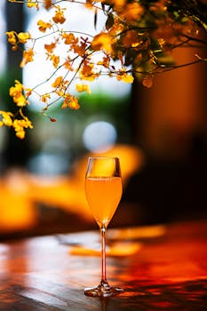 A sophisticated cocktail glass with orange drink adorned by yellow flowers, set in a Tokyo bar's ambient lighting.
