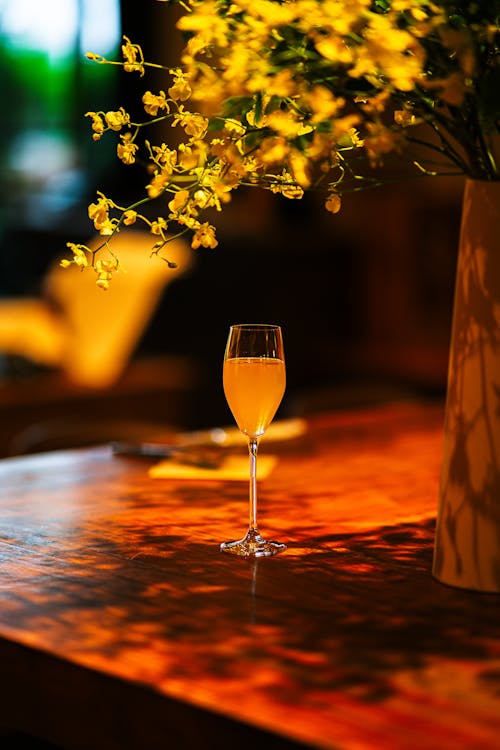 A glass of champagne sits on a table with yellow flowers