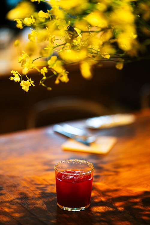 A glass of red drink sitting on a table with yellow flowers