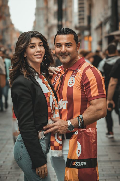 Free A happy couple in Galatasaray jerseys posing on a bustling city street, spreading joy and celebrating togetherness. Stock Photo