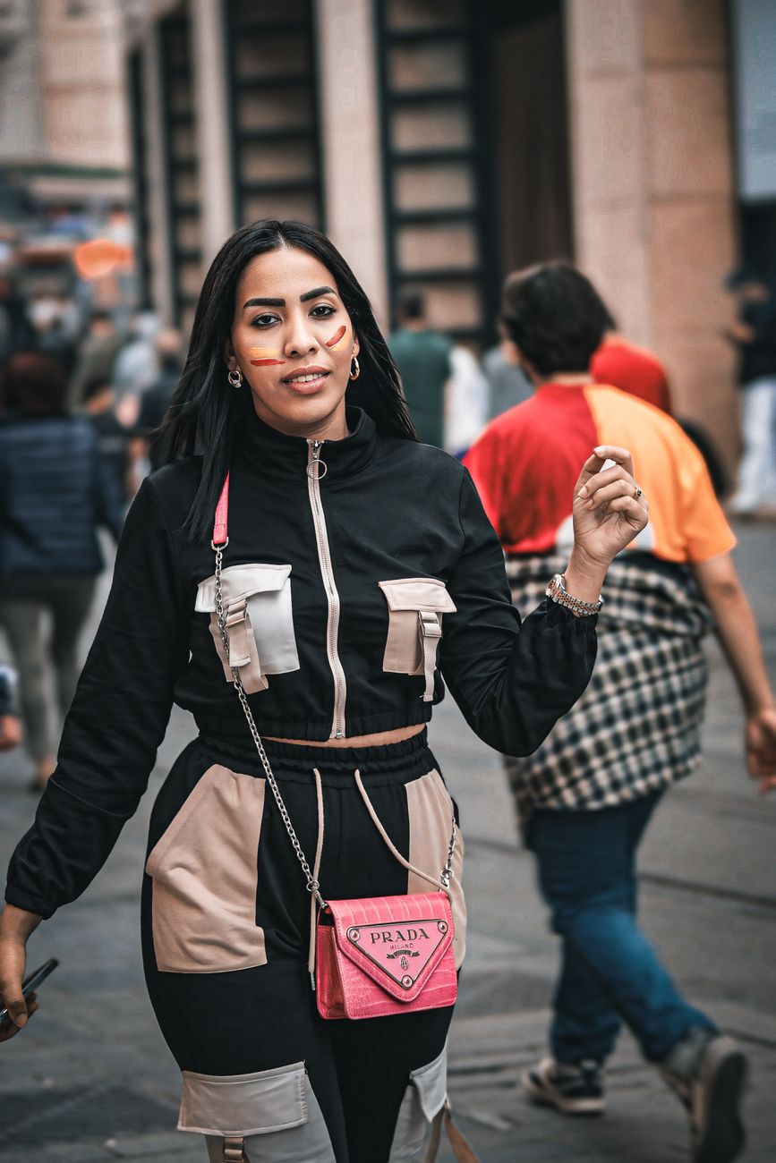 Confident woman walks on a bustling city street, showcasing modern fashion with a stylish purse.
