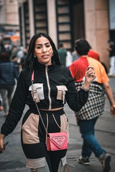 Confident woman walks on a bustling city street, showcasing modern fashion with a stylish purse.