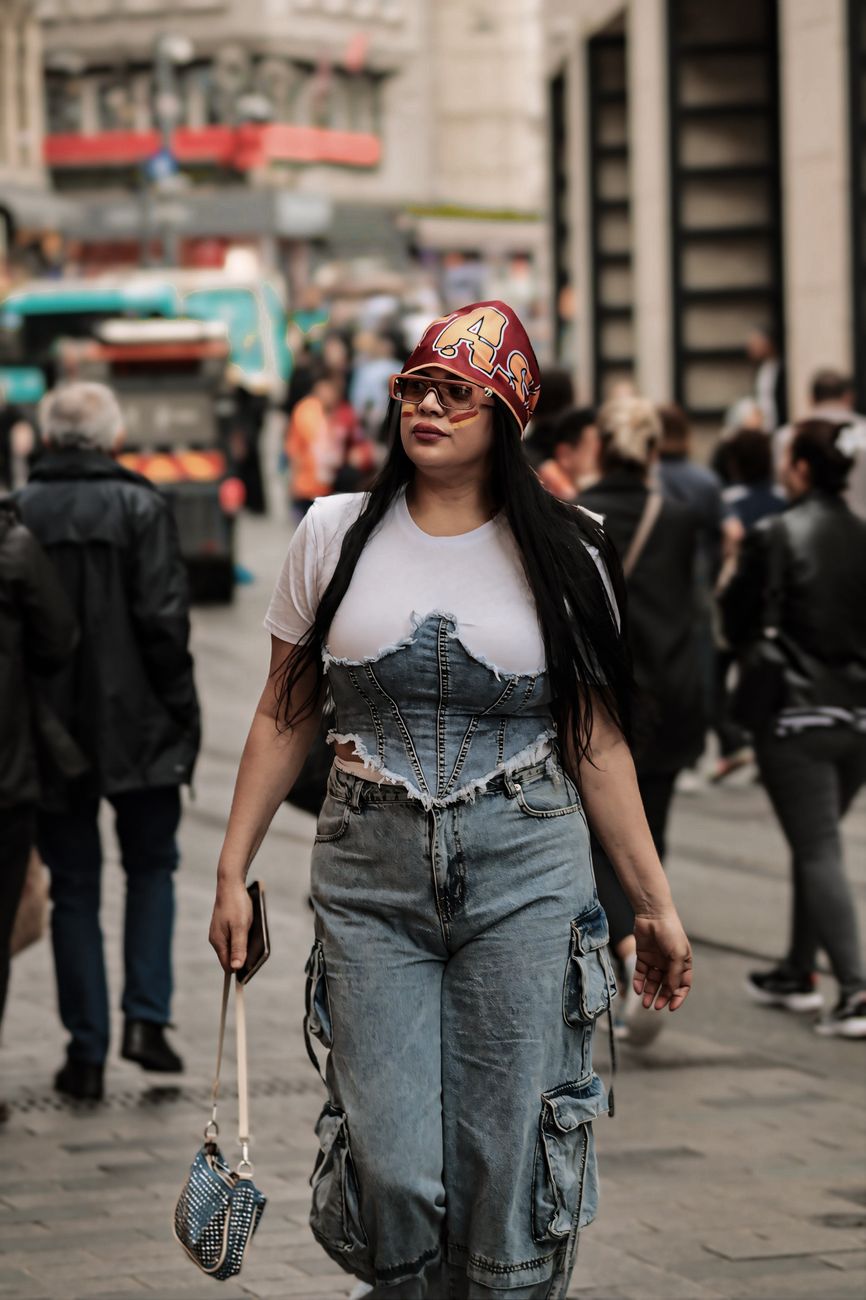 A stylish woman in denim and a headscarf walks confidently down a bustling city street.