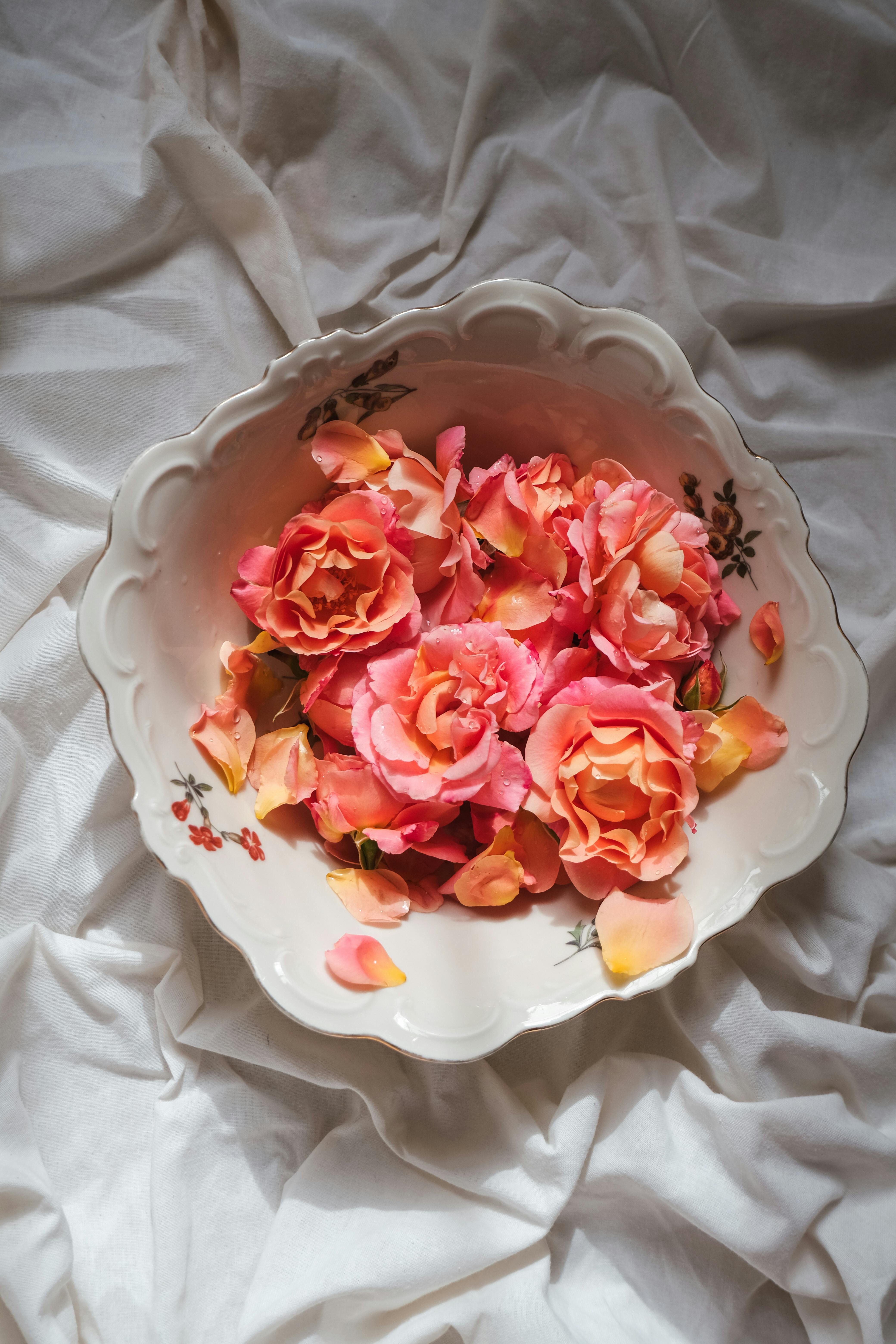 Aesthetic arrangement of pink rose petals in a decorative bowl on a white sheet, evoking romance.