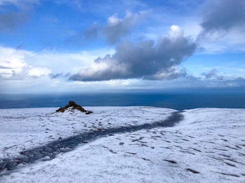 A snow covered hill with a path leading to the ocean