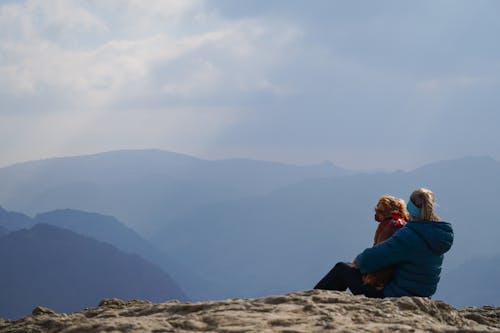 A woman and a child sitting on a rock overlooking the mountains