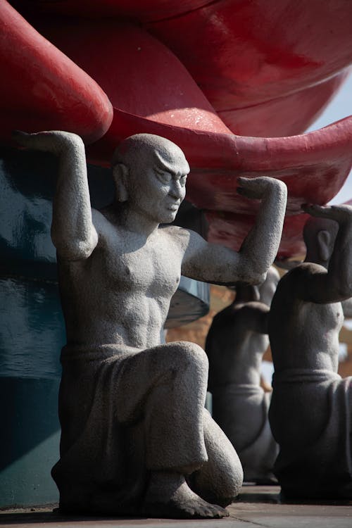 Statues of men holding up a large red object