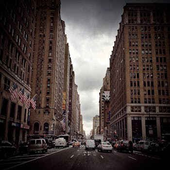 在纽约市繁忙的大道上，街景中有摩天大楼、美国国旗和多云天空下的车流