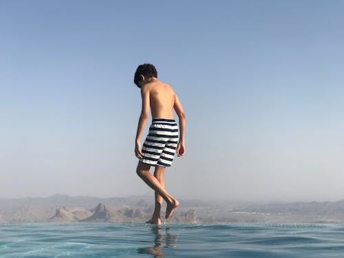 後視圖的男孩穿著泳褲站在無邊泳池的邊緣