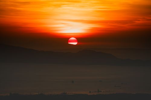 Free A breathtaking sunset over the ocean, casting dramatic colors and highlighting mountain silhouettes. Stock Photo